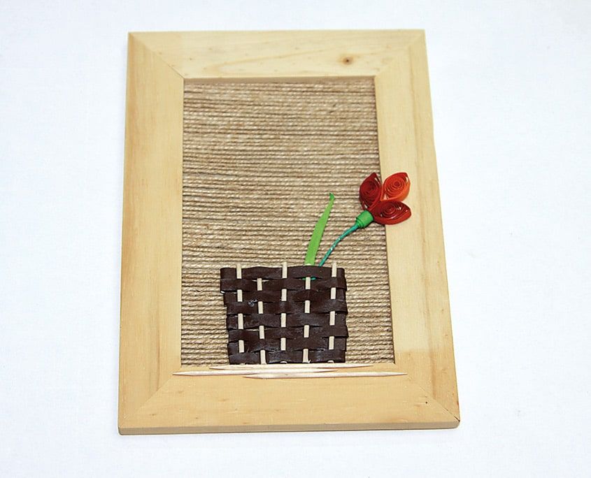 Ahşap çerçevedeki örgü kağıt sepetten yükselen yeşil saplı kırmızı quilling lale