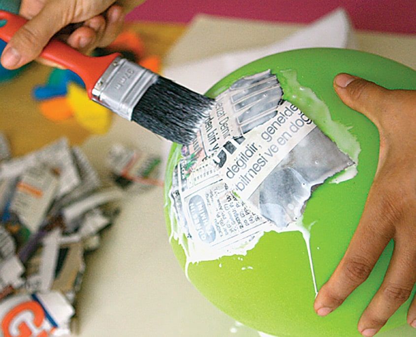 Tutkallı yeşil balonun yüzeyine gazete kağıdı parçaları fırçayla bastırılarak yapıştırılıyor
