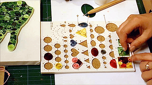 Daire, damla ve kalp kalıplı quilling panosunda bir elin hazırlanan renkli rulo parçalarını yerleştirmesi