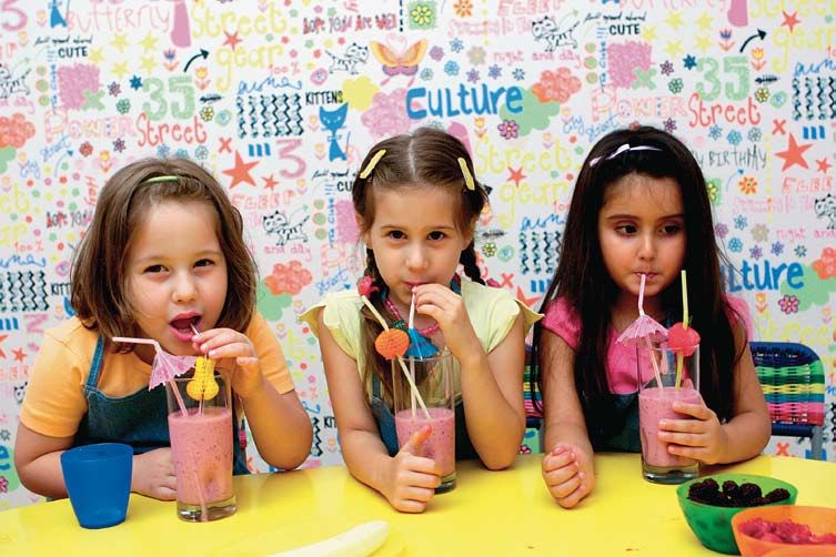 Meyve kokteylleri: pipetli pembe meyve kokteyllerini içen üç çocuk, renkli masa başında