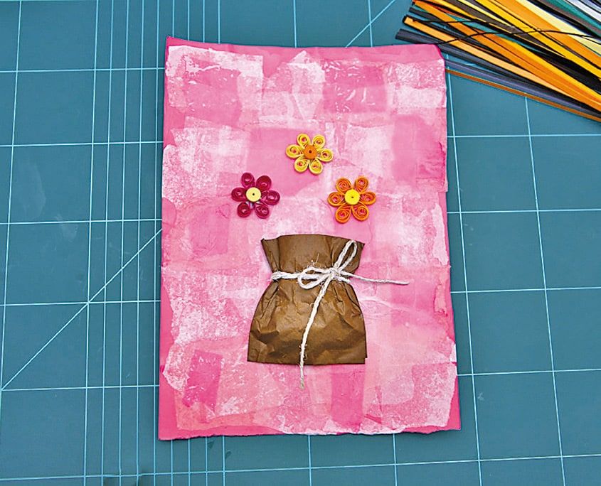 Pembe pelür zemine yapıştırılan kağıt çuval saksının üstüne quilling çiçekler yerleştiriliyor