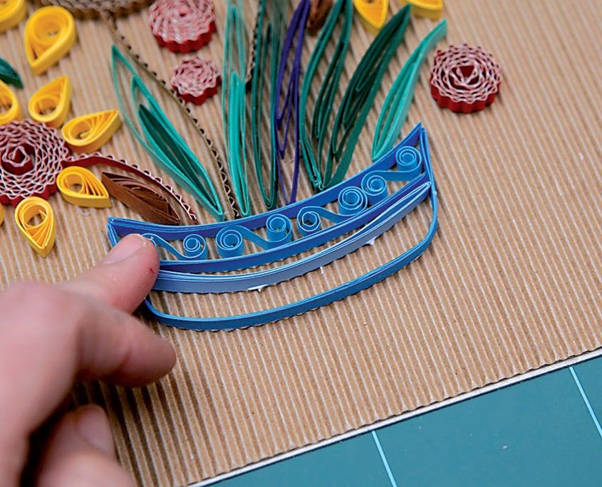 Mavi vazonun içi kıvrımlı quilling süslerle doldurulmuş, üstünde yeşil yapraklar yükseliyor