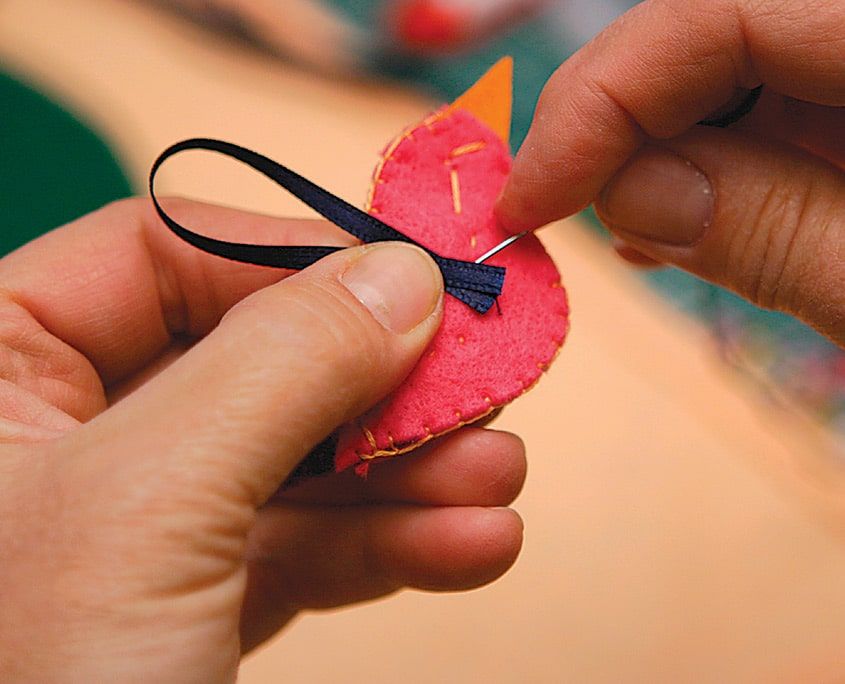 Dikişi biten pembe keçe kuşa asmak için lacivert kurdele ilmek takılıyor