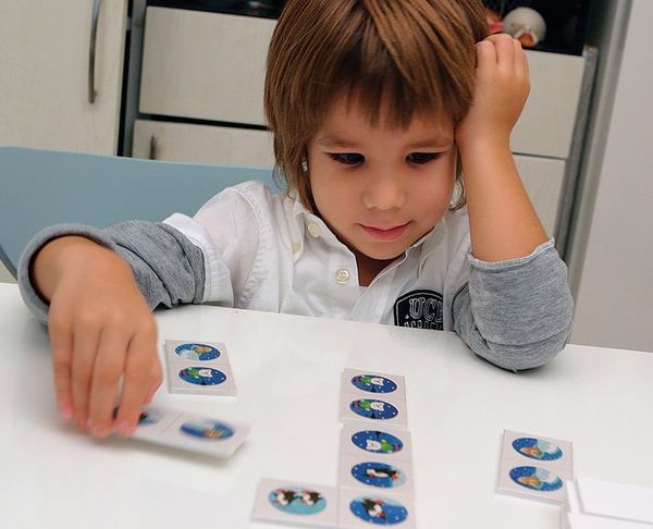 Kartona yapıştırılmış resimlerle yapılan resimli domino: masada taşları sıraya dizen bir çocuk