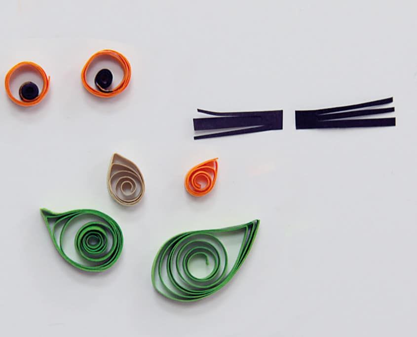 Hazırlanmış quilling parçaları: turuncu göz halkaları, siyah şerit bıyıklar, damla ve yeşil yapraklar