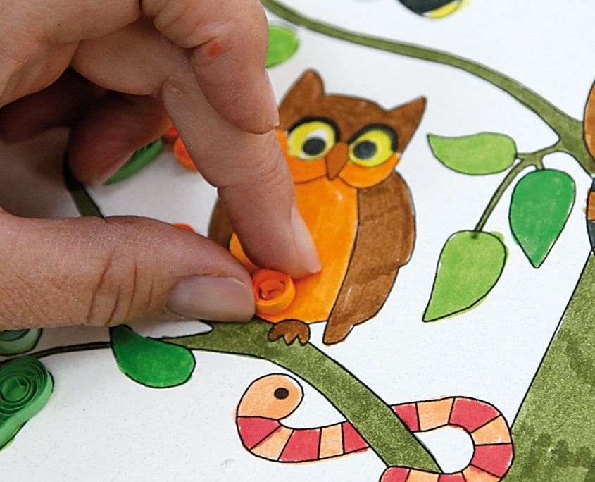 Boyalı ağaç çiziminin üstündeki turuncu baykuşun gözüne quilling rulosu parmakla yerleştiriliyor