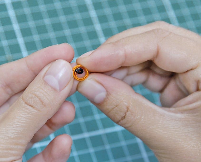 Siyah merkezli sıkı turuncu quilling rulosu parmak uçları arasında tutuluyor