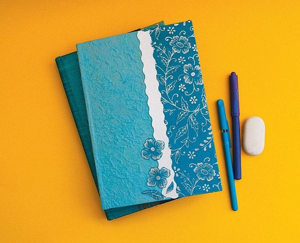 Kitap ve defter kaplama fikri: kabartma desenli turkuaz kağıtla kaplanmış defter, dantel şerit, kalemler ve silgi