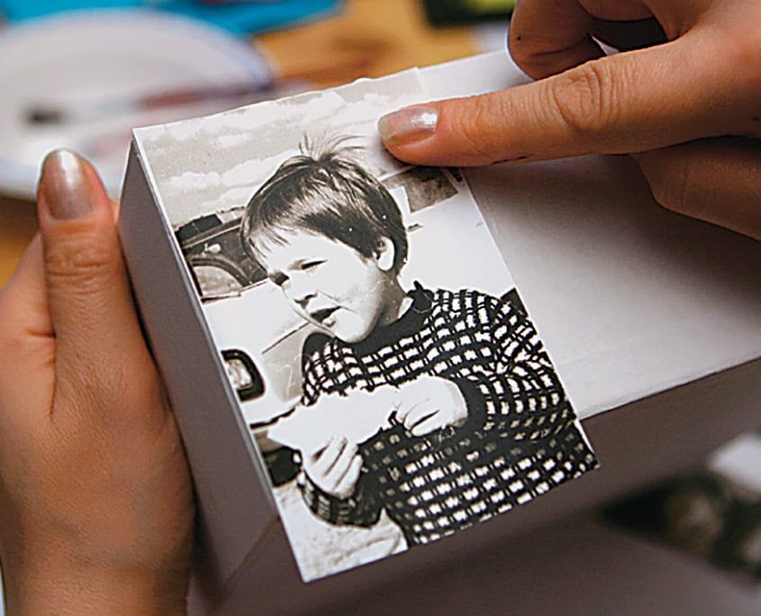 Siyah beyaz bir çocuk fotoğrafı yapıştırıcı sürülmüş kutu yüzeyine parmaklarla bastırılıyor