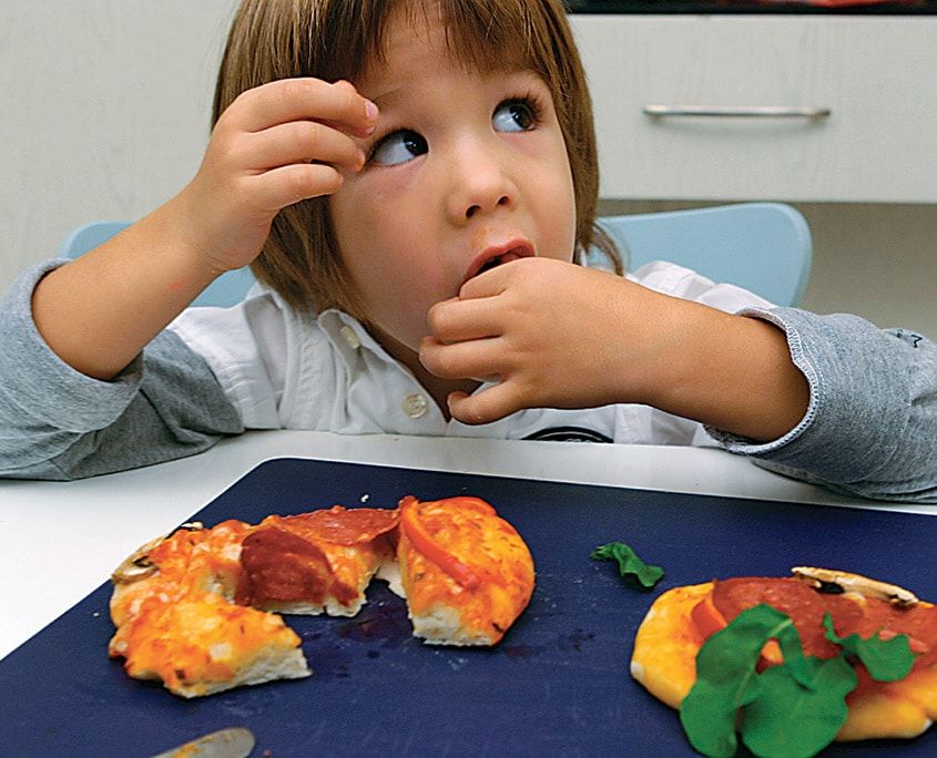 Yarısı yenmiş pişmiş mini pizzaların başında pizzasını yiyen bir çocuk