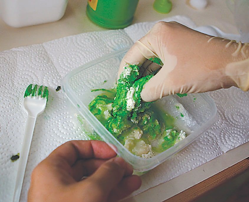 Eldivenli el un, tuz ve yeşil boyayı plastik kapta yoğuruyor, yanda plastik çatal duruyor