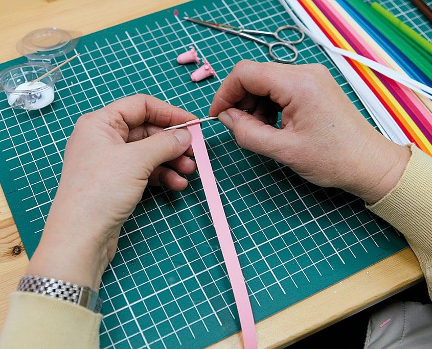 Pembe şeridin ucu ince bir çubuğa takılarak sarılmaya hazırlanıyor, arkada renkli şerit demeti