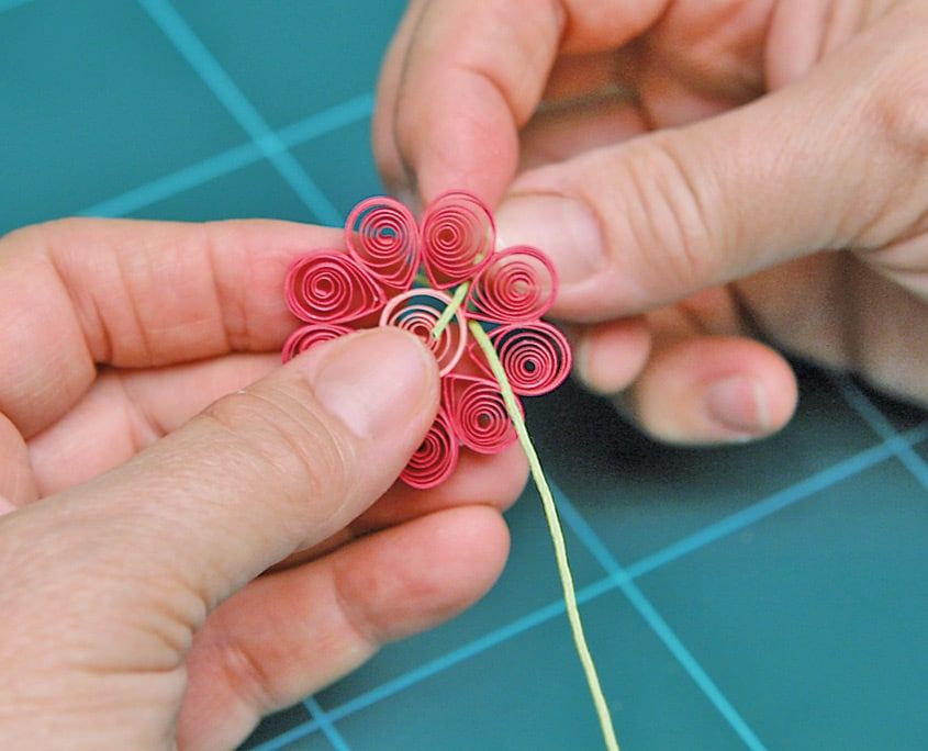 Açık yeşil ip pembe quilling çiçeğin ortasında düğümlenmek üzere parmaklarla çekiliyor