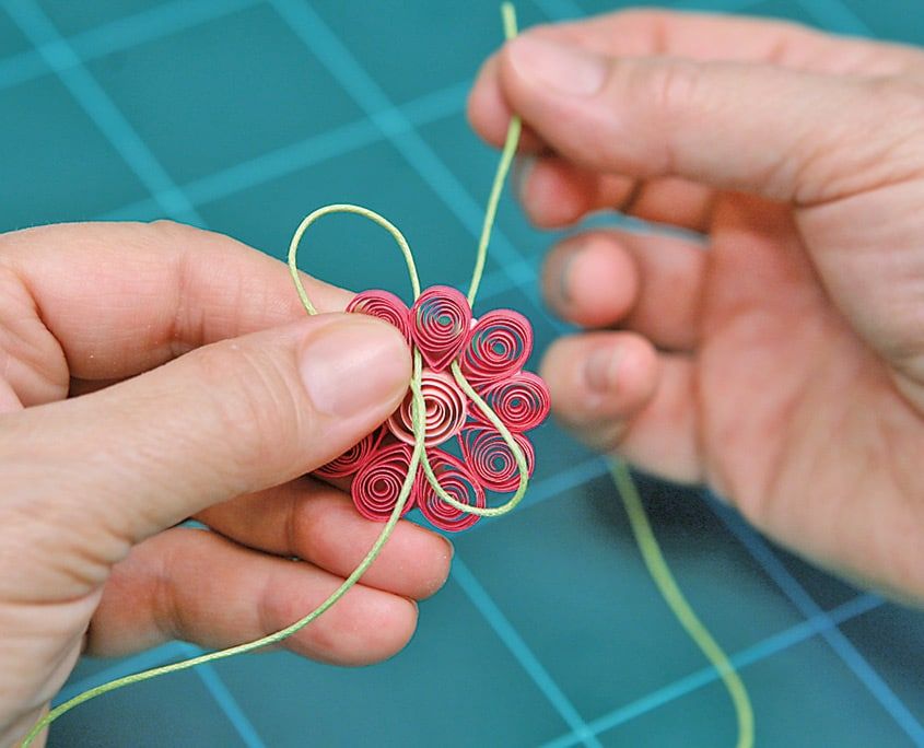 Pembe quilling çiçeğin arkasından ip ilmeği çevrilerek kolye askısı hazırlanıyor