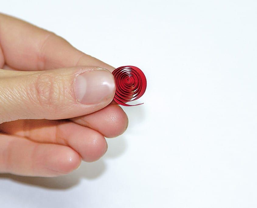 Parmaklar arasında gevşek sarılmış kırmızı quilling spirali, lale yaprağı için hazır