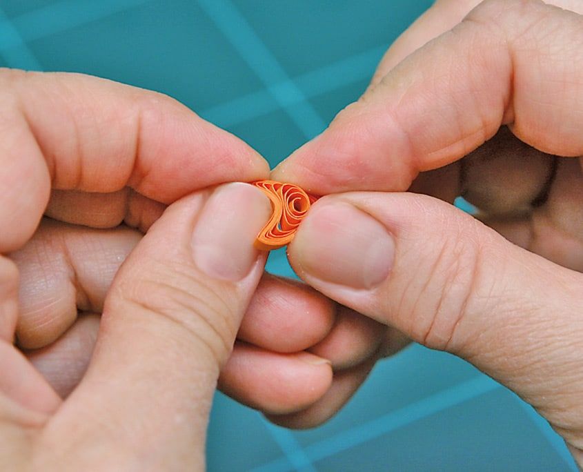 Turuncu quilling spiralinin bir ucu parmaklarla bastırılarak damla biçimi oluşturuluyor