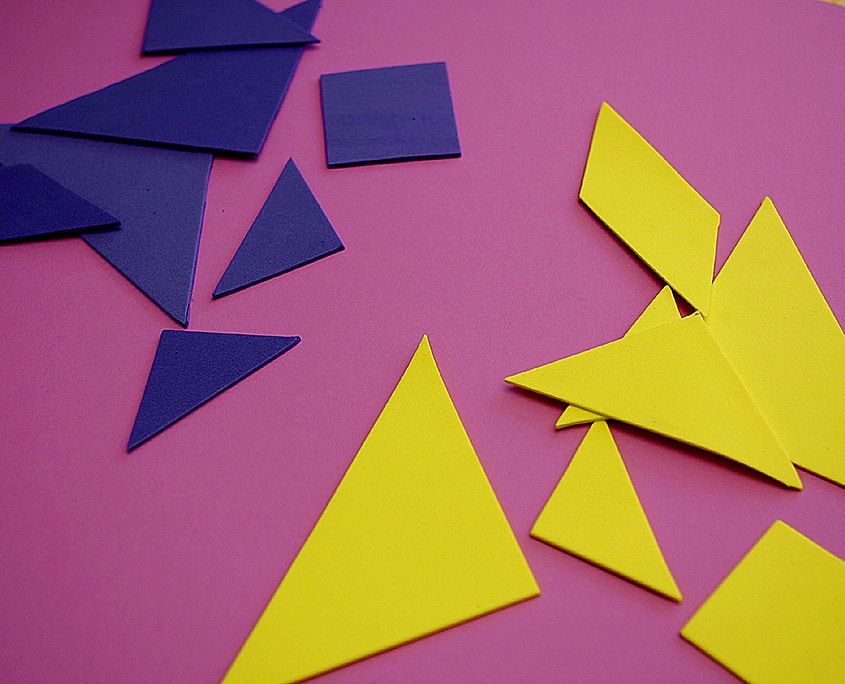 Pembe zemine dağılmış sarı ve lacivert tangram üçgenleri, kare ve paralelkenar parçaları