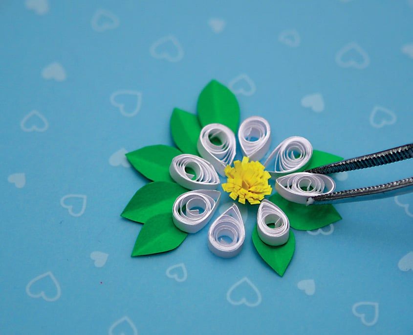 Cımbızla yerleştirilen beyaz damla yapraklı, sarı saçak göbekli quilling papatya, yeşil yaprakların üstünde