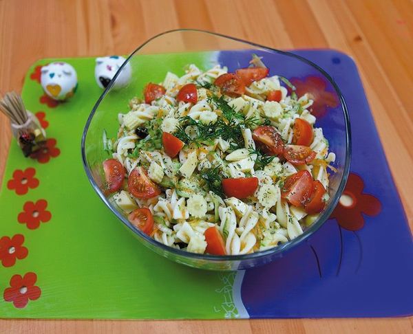 Makarna salatası: cam kasede burgu makarna, çeri domates ve dereotu, yeşil çiçekli amerikan servis üstünde