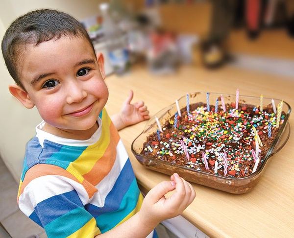 Mozaik pasta: renkli şeker serpilmiş, mumlarla süslü mozaik pasta cam tepside, yanında bir çocuk