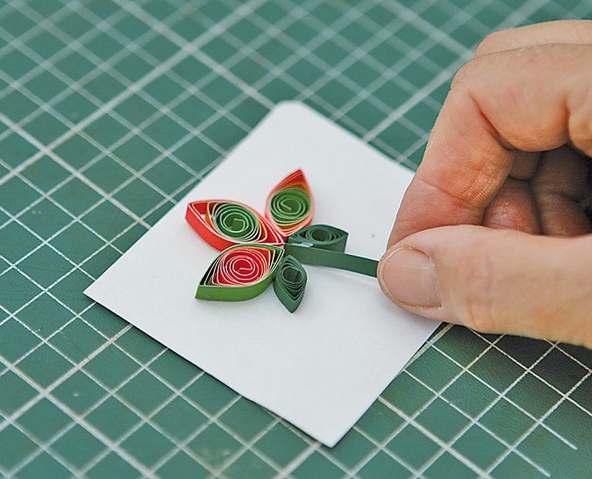 Kırmızı-yeşil quilling lalesine yeşil kağıt şeritten sap eklenirken parmakla bastırılıyor