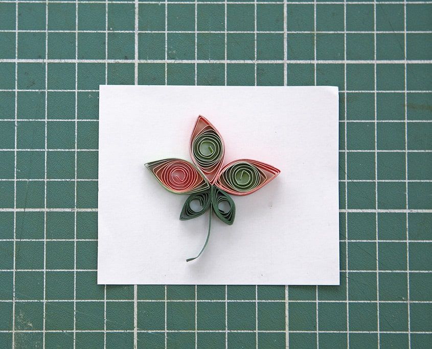 Beyaz kart üzerinde tamamlanmış kırmızı-yeşil quilling lale, kıvrık yeşil sap ve iki yaprak