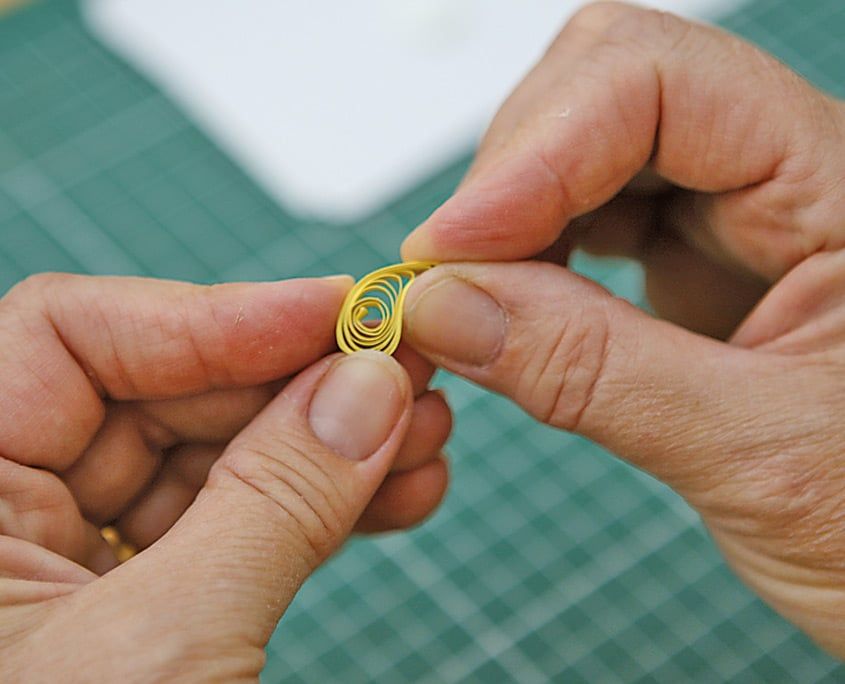 Sarı quilling şeridinden sarılmış gevşek rulo parmaklar arasında tutuluyor