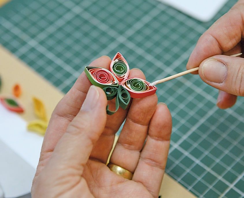 Kırmızı-yeşil quilling çiçek parmak ucunda tutularak arkasına kürdanla yapıştırıcı sürülüyor