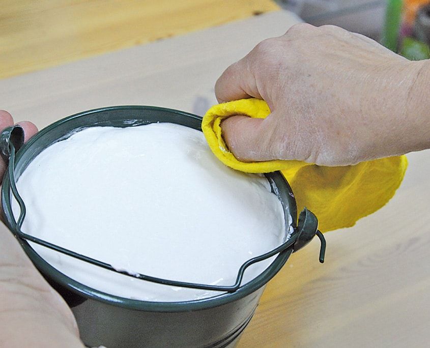 Beyaz dolgu malzemesiyle doldurulmuş koyu yeşil metal kovanın kenarı sarı bezle siliniyor