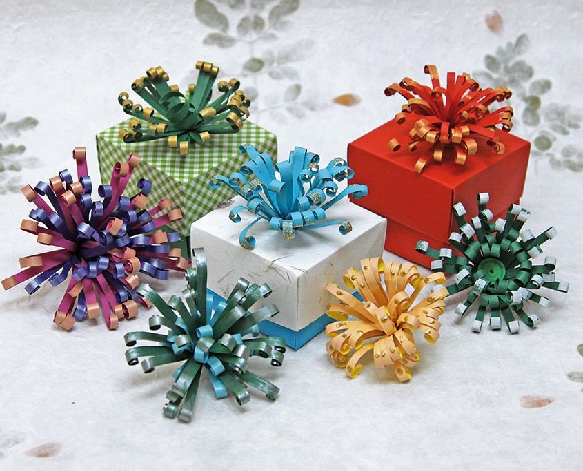 Quilling ile paket süsleri: hediye kutularının üstünde mor, mavi, yeşil ve sarı püsküllü kağıt fiyonklar