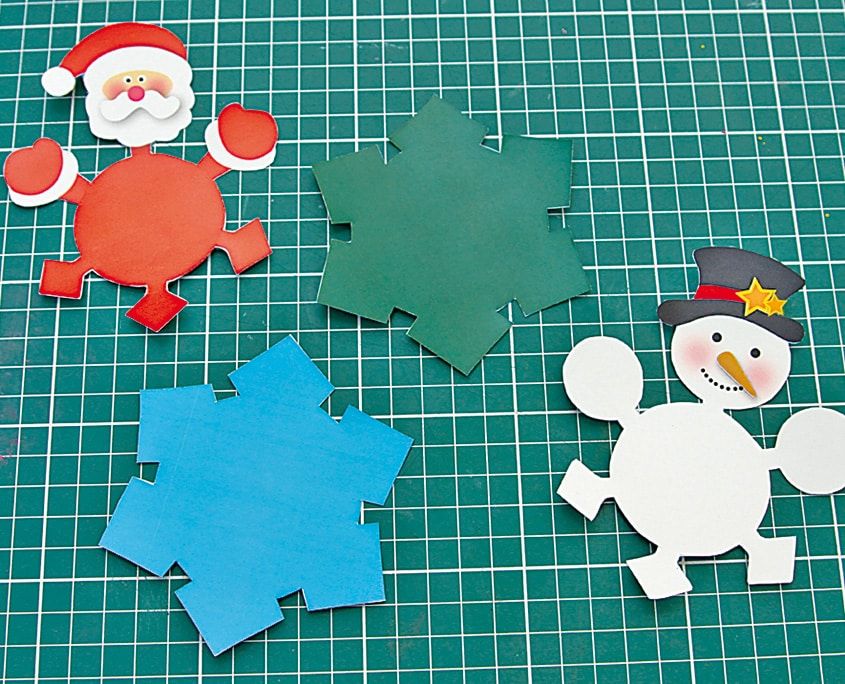 Şablondan kesilmiş Noel Baba, kardan adam, yeşil ve mavi kar tanesi karton parçaları
