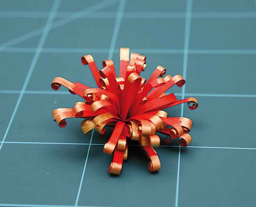 Kesim matı üzerinde uçları altın kıvrımlı, açılmış kırmızı püsküllü quilling paket süsü