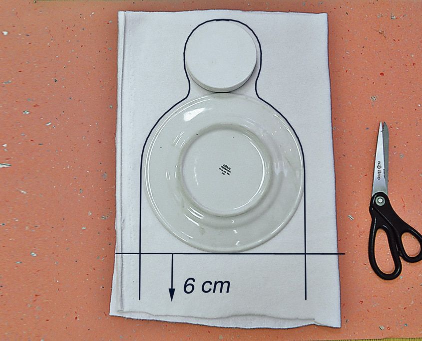 İkiye katlanmış beyaz polar üzerine tabak ve kapak yerleştirilip bere kalıbı çiziliyor, alt kısım 6 cm