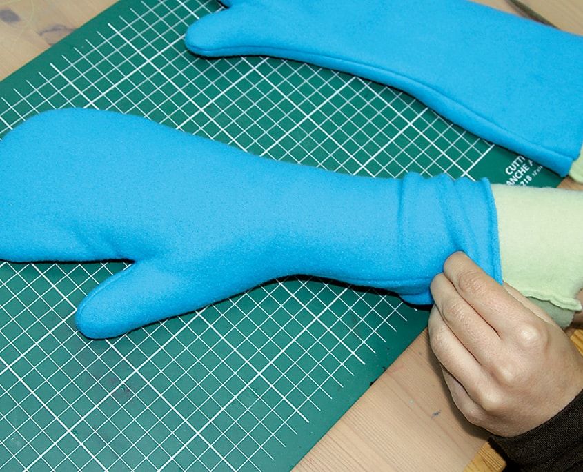 Bir el açık yeşil astarı mavi polar eldivenin içine yerleştiriyor