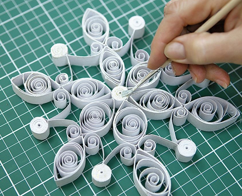 Tamamlanmak üzere olan beyaz quilling kar tanesine kürdanla son süslerin yapıştırılması