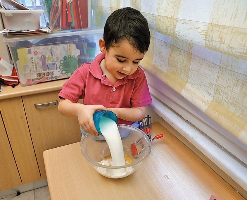 Bir çocuk krep hamuru için cam kaseye ölçü kabıyla un döküyor