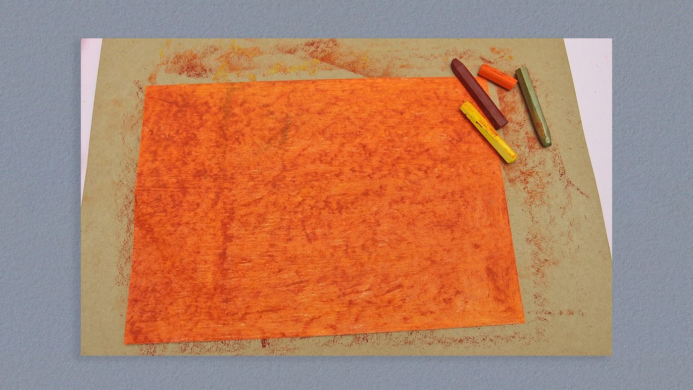 Turuncu pastel boyayla baştan sona boyanmış kağıt, yanında pastel boya parçaları