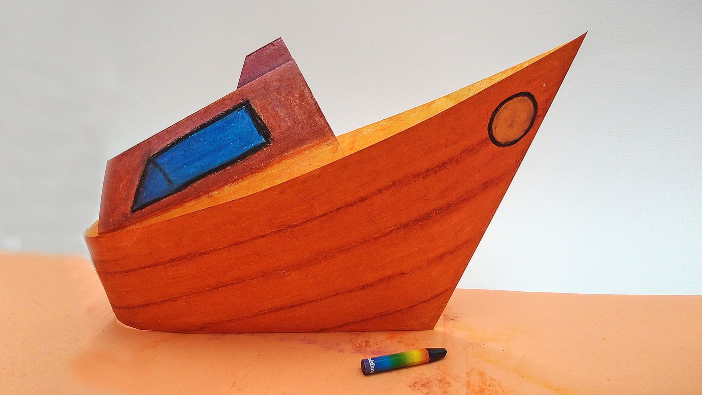 Tamamlanmış origami tekne turuncu kum zeminde duruyor, önünde bir pastel boya