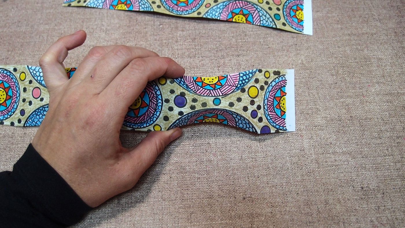 Katlama izi çizilen desenli kağıt şerit elle bükülerek ortasından kavis veriliyor