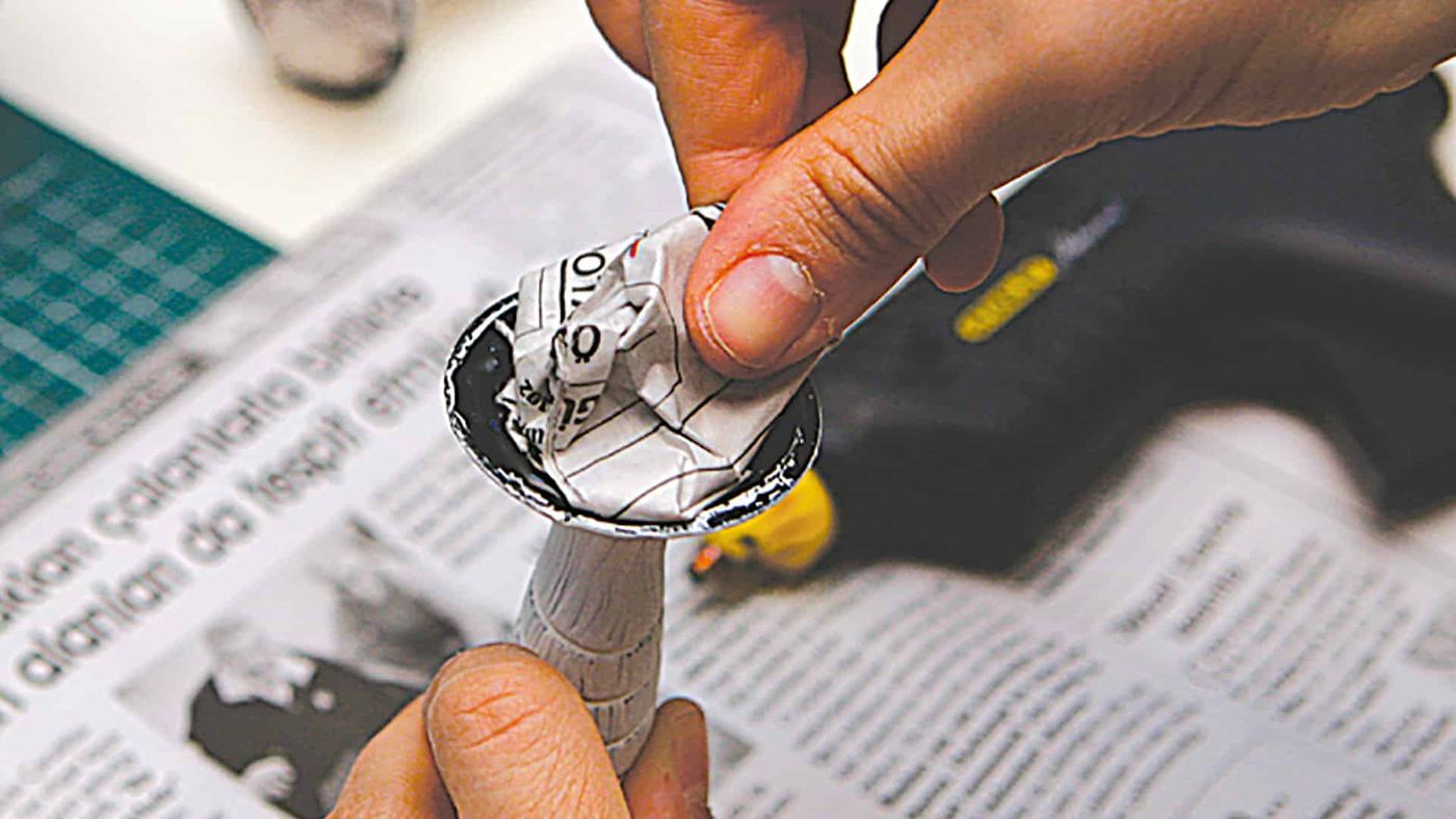 Plastik sap sıcak silikon tabancasıyla kağıt topun deliğine yapıştırılıyor, gazete üzerinde
