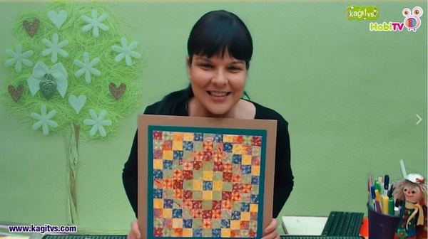 Canlı atölye yayınından kare: eğitmen desenli kağıt karelerden yapılmış çerçeveli kağıt kırkyama panoyu gösteriyor