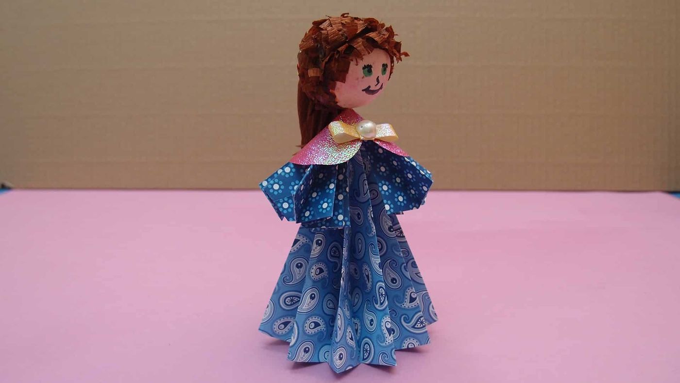 Kahverengi saçlı origami bebek hafif yandan, pembe parlak yaka ve fiyonklu mavi desenli elbise