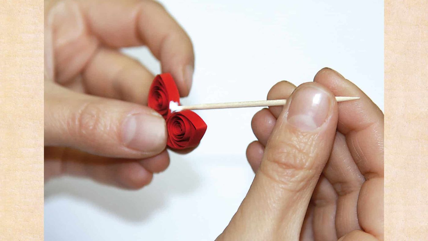 Kürdanın ucunda birleştirilen kırmızı quilling taç yapraklar, iki elle tutuluyor