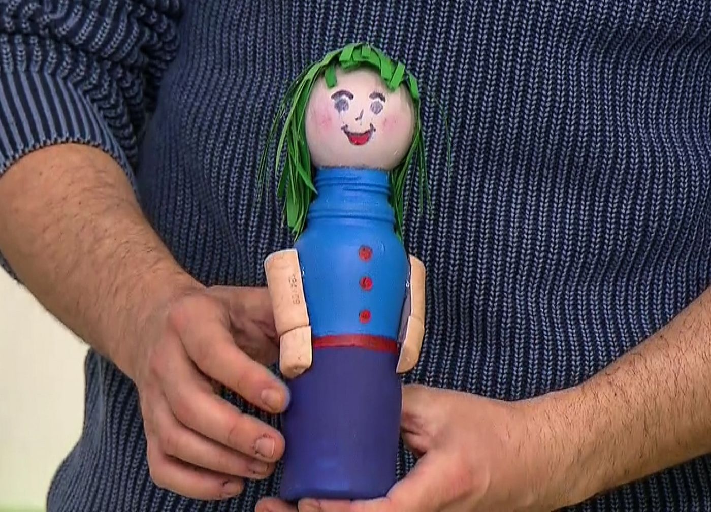 Yakın plan: elde tutulan yeşil yün saçlı, mavi gövdeli, mantar kollu plastik şişeden bebek