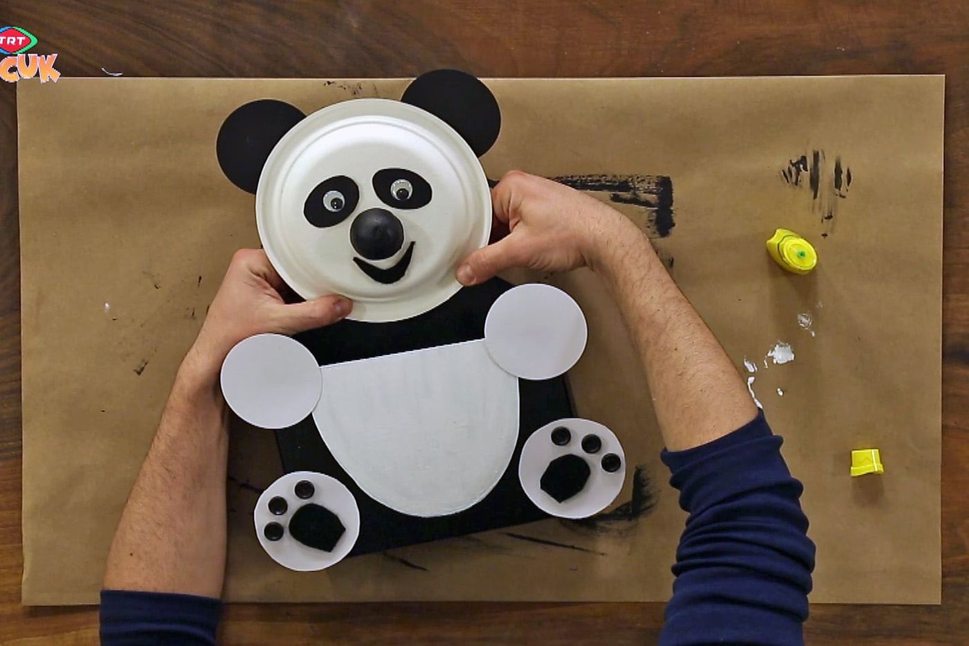 İki el kağıt tabaktan panda yüzünü siyah kartondan gövdeye yerleştiriyor, beyaz karın ve patiler hazır