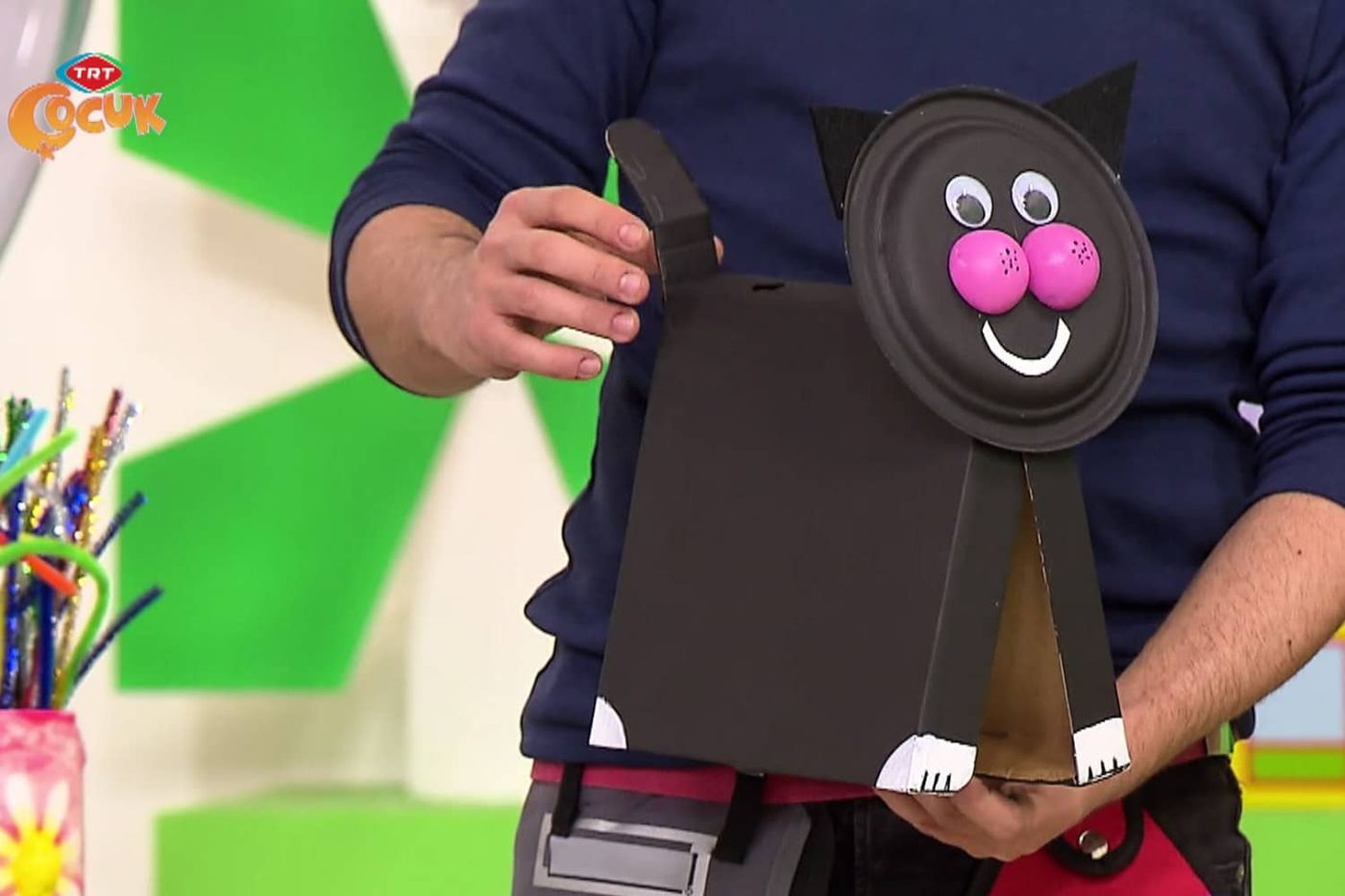 Sunucunun elinde kağıt tabak yüzlü, pembe ponpon yanaklı siyah karton kedi dosyalık