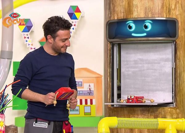 Mini davul: programdan kare, sunucu elinde kırmızı kutudan yapılmış davulla stüdyoda duruyor