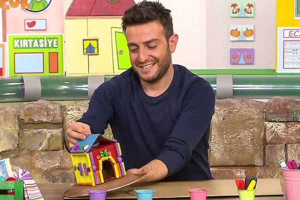 Makarna ev: stüdyoda sunucu renkli makarnalarla süslenmiş karton evi gösteriyor, video karesi