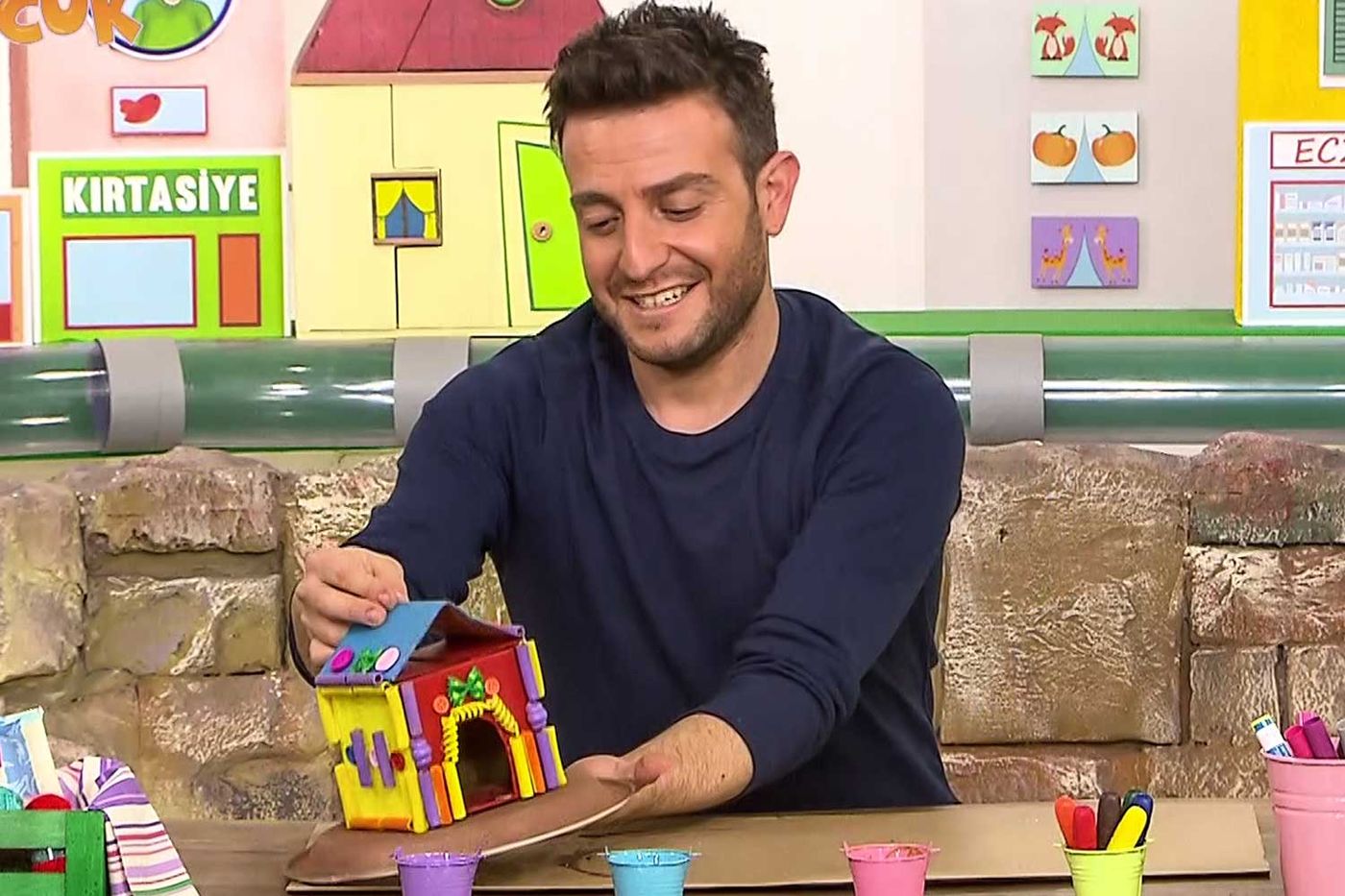 Makarna ev: stüdyoda sunucu renkli makarnalarla süslenmiş karton evi gösteriyor, video karesi