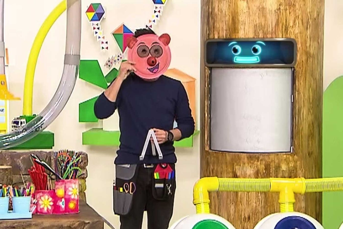 Programdan kare: sunucu stüdyoda kağıt tabaktan yapılmış pembe ayı maskesini yüzüne tutuyor